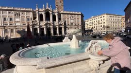 A woman drinks water at the fountain in Piazza Santa Maria Maggiore, restored for the Jubilee, and in the background, the Papal Basilica of Santa Maria Maggiore in Rome.