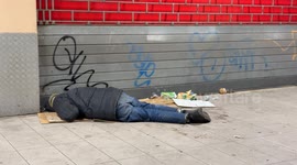 A homeless man sleeps on the floor in front of a closed shop shutter in a suburban area of Rome.