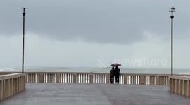 Two people on the Ostia pier look at the very rough sea on the coast of Lido di Ostia in Rome.