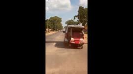 Tuktuk hanging from back of minivan bounces along road