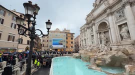 Wide view of Piazza Fontana di Trevi with the Trevi Fountain on the right and in the background citizens and tourists with umbrellas attending the inauguration of the Trevi Fountain following the cleaning work for the Jubilee on a rainy December day in Ro