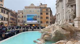 Medium shot of Piazza Fontana di Trevi with the Trevi Fountain on the right and in the background citizens and tourists with umbrellas attending the inauguration of the Trevi Fountain following the cleaning work for the Jubilee on a rainy December day in