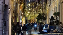 People walk in an alley in the center and above them the decorations with Christmas lights during the Christmas period in Rome.