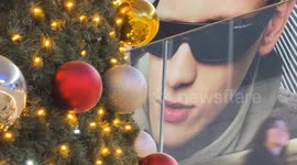 A poster depicts a man with giant sunglasses who, like a big brother, seems to look down on the people passing by and the decorated Christmas tree inside Termini Station during the Christmas period in Rome.