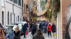 People coming and going in one of the alleys of Trastevere and, on the left, you can see 4 people who participated in the Christmas lunch for the poor in Santa Maria in Trastevere, organized by the Community of Sant'Egidio on Christmas Day in Rome.