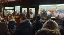 The doors closing in front of people in winter clothes on a bus leaving the bus stop packed with people, in Rome.