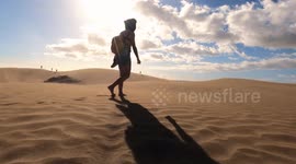 Dune against seascape, desert near seashore. Tourists walking thorugh the dunes of Maspalomas in Gran Canaria during a windy day.