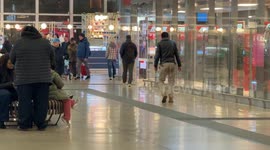 A staggering, limping man in dirty trousers walks away inside Termini Station in Rome.