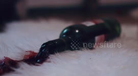 Close up: Red wine bottle is spilled on a white furry bedroom floor during nighttime.