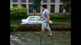 Man walks on stilts to cross flooded road