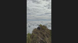Hiker looks out over sea of clouds from mountain peak