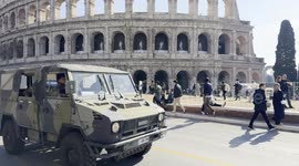 An army van crosses the scene while tourists are stationed in the square in front of the Colosseum in Rome.