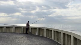 An elderly man is fishing on the Lido di Ostia pier on a February morning with calm seas and a grey sky that allows a few rays of sunshine to be glimpsed, in Rome.