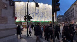 Many people in the evening cross the intersection of Piazza Venezia and in the background the installation of the mural “The Constellations of Rome” by the artist Pietro Ruffo, on the silos of the construction site of the Metro C stop in Rome.