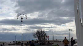 An airplane crosses the sky and dips behind some buildings in Lido di Ostia to land at Fiumicino airport on a cloudy February day in Rome.