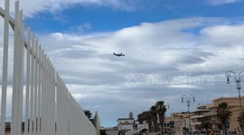 An airplane crosses the sky and dips behind some buildings in Lido di Ostia to land at Fiumicino airport on a cloudy February day in Rome.