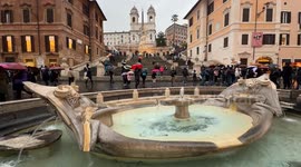 The Barcaccia in Piazza di Spagna and in the background the Spanish Steps with the Bulgari Christmas tree and tourists walking with umbrellas on a rainy day just before the Christmas holidays in Rome.