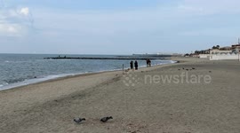 People stroll as pigeons search for food on the beach with some garbage along the coast of Lido di Ostia on a cloudy day in February in Rome.