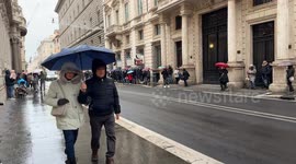 An ambulance with sirens blaring travels along Via del Corso during an emergency on a rainy winter day in Rome.