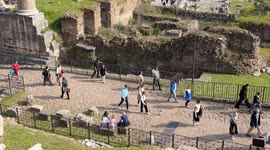 Wide vertical movement overview of the Roman Forum visited by many tourists on a day with spring temperatures in February in Rome.