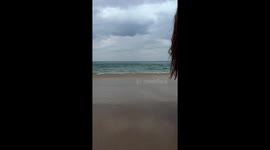 Woman's beachside pose interrupted by sudden wave in Phuket, Thailand