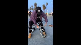 Man rides bike with guitar body and surprises bystanders in Venice Beach, California, USA