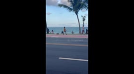 Elderly lady walks dog on skateboard along beach in Brazil