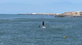 A man rows away standing on his surfboard near the coast of Lido di Ostia with calm sea and clear skies on a Sunday morning in Rome.