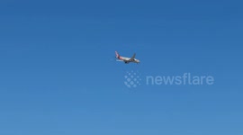 An American Airlines plane flies through the blue sky as it prepares to land at Fiumicino Airport and disappears behind some buildings in Rome.