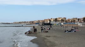 Tourists on the beach of Lido di Ostia with calm sea and sky covered with white clouds on a March day in Rome.