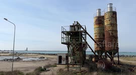 The old concrete production plant and in the background the old lighthouse and the stretch of sea where some people practice wing foiling in the area where the creation of the cruise tourist port is planned in Fiumicino near Rome.