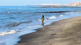 A metal prospector with boots and a metal detector searches for precious objects along the Lido di Ostia beach on a beautiful March day in Rome.