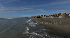 Wide shot of the waves on the coast as a man looks out to sea and his son plays with a ball on the beach of Lido di Ostia on a clear day in March in Rome.