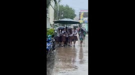 Schoolgirls shelter under giant umbrella during rainstorm