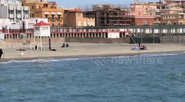 A beach towel vendor tries to sell a beach towel on a breezy March day on the beach at Ostia Lido in Rome.
