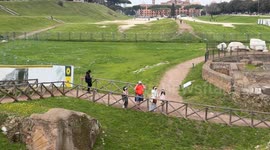 Wide shot of tourists with immersive headsets with see-through augmented and virtual reality technology taking a virtual tour of Ancient Rome and the Circus Maximus in the background in Rome.
