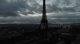 An incredible aerial shot of the Eiffel Tower at dusk, standing tall against the backdrop of Paris. The cloudy sky and soft evening lights create a cinematic and moody atmosphere, offering a unique perspective of the city’s iconic landmark.