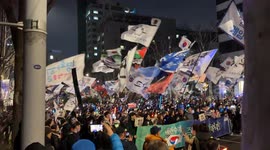 The people of Seoul, South Korea stand up and protest in the streets of the capital city (landscape video). Flags are waved in sync as loud music plays.