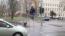 A street performer in Berlin entertains drivers at a busy intersection by juggling clubs while balancing on a ladder during a red light.