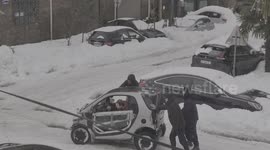 People Help Push A Mini Car Out Of The Snow