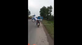 the man driving a motorbike carrying another motorbike on the back moving on the road