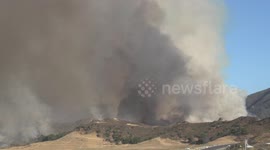 heavy black smoke rises from hillside fire at