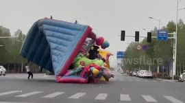 Bouncy castle blown away by wind drags pedestrians across intersection