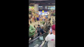 Dinosaur rides escalator alongside bemused shoppers