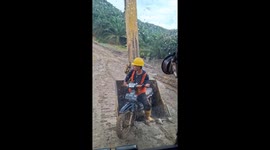 Rescuing a worker on a motorcycle from the mud by excavator arm in East Kalimantan