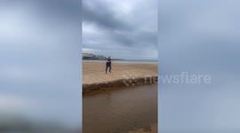 Funny moment man falls short attempting to jump across beach trench and takes a tumble