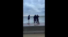 Wave splashes friends at boardwalk in Comodoro Rivadavia, Argentina