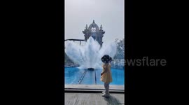 Scared little girl falls to ground as water from theme park ride crashes against glass barrier