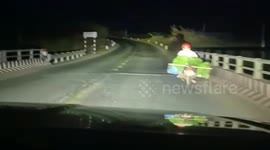 Driver shines headlight to help motorcycle rider navigate dark road