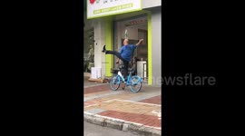 Elderly cyclist rides with just 1 hand and foot while balancing water bottle on head